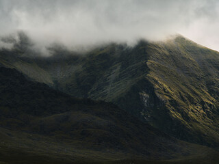 Misty mountains shrouded in atmospheric haze. Sunlight highlights a stark mountain ridge.
