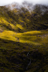 A scenic mountain view with grassy ridges, rocky outcrops, and deep shadow contrasts.