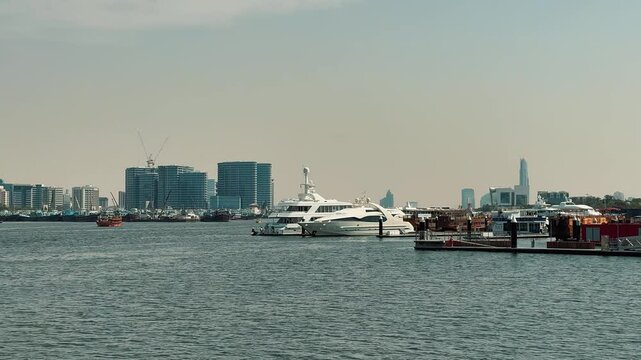 Scenic panning shot of Dubai Creek featuring the Deira skyline with modern skyscrapers and traditional wooden dhow boats docked along the sunny waterfront in United Arab Emirates.

