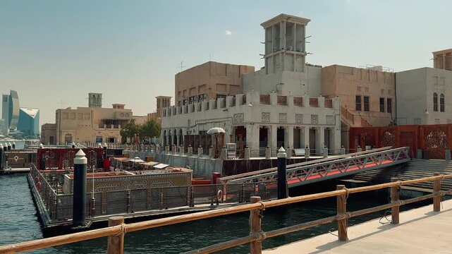 Scenic views of Dubai's Al Seef heritage district featuring traditional Arabian architecture, wind towers, narrow alleyways, and waterfront scenery along the creek during a sunny day.

