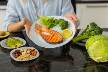 Woman holds plate with grilled salmon broccoli lettuce and lemon for keto lunch at home kitchen....