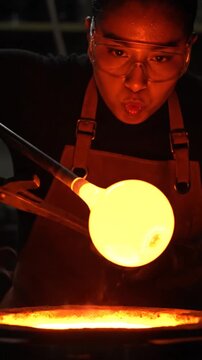 Skilled glassblower carefully heating molten glass in a workshop furnace.