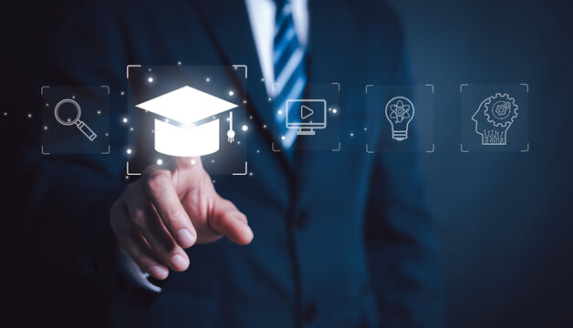 Businessman selecting online education icon with graduation cap on virtual interface, digital learning, e learning technology, knowledge development, training course and smart education concept.