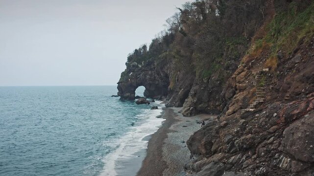 Aerial and scenic view of Delikli Tas beach and its natural rock arch in Giresun, Turkiye. Dramatic Black Sea coastline with steep cliffs and autumn colors.