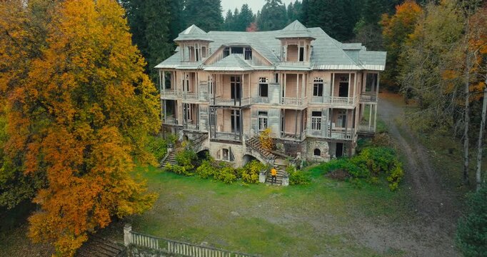 Abandoned historic Stalin's summer house in Racha, Georgia; camera zooms into the building, rises to roof level, and then pans toward the scenic autumn forest.