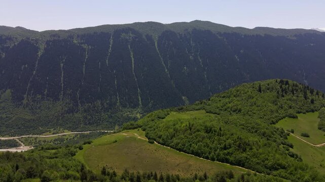 Aerial pan along an alpine valley in Upper Svaneti, Georgia, with terraced meadows, clustered villages, a braided river, a winding road, and Shkhara under clear summer light.