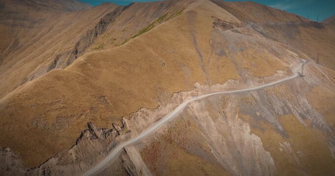 Aerial view of a white car driving on the steep slopes of Abano Pass, Georgia. The camera performs a forward and right-curving drone movement following the vehicle.