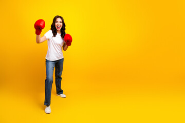 Young woman with boxing gloves poses in a bright yellow studio smiling ready for fitness and...