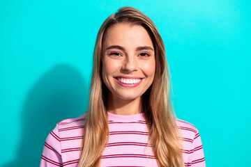 Fototapeta premium Happy young woman with blonde hair wearing pink striped shirt smiles against teal blue background for lifestyle fashion stock image