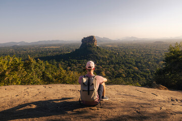 Tourist with backpack sittng on Pidurangala Rock and looking at Sigiriya Rock. Travel adventure and...