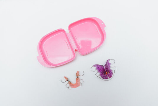 Orthodontic retainers and removable dental plates for teeth alignment with pink storage case isolated on white background, pediatric dentistry and stomatology concept