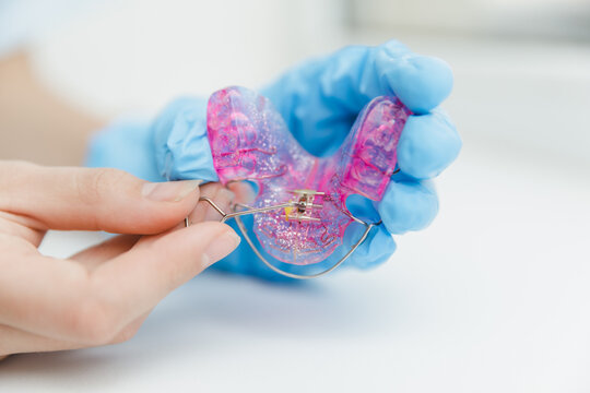 Orthodontist hand in blue glove using special key to adjust expansion screw on pink dental plate, professional orthodontic appliance activation concept