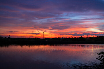 Obraz premium Vibrant Twilight Sunset Glow Reflecting Over Calm Lake Water,A breathtaking sunset scene featuring a dramatic sky filled with orange, purple, and blue hues, perfectly reflected on the tranquil surface
