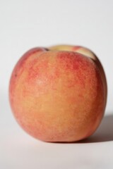 Ripe peach isolated on light background. Fresh whole peach with natural red and yellow skin texture, soft surface and subtle shadow. Minimal studio fruit photography, healthy summer food concept.