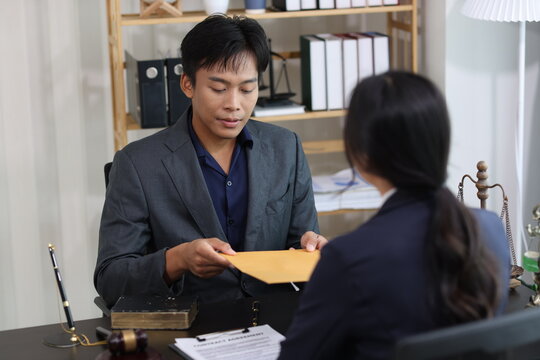 Asian lawyer handing over confidential legal documents to business client during a private meeting in law firm office, discussing contract agreement terms and conditions.
