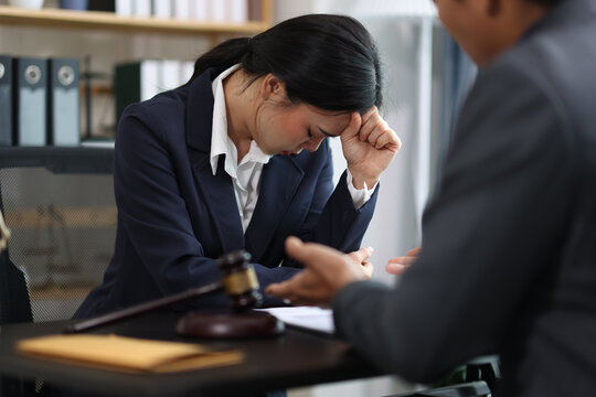 Stressed businesswoman suffering from headache after receiving bad news from her lawyer during legal consultation in office, lawyer is explaining lawsuit details to client.