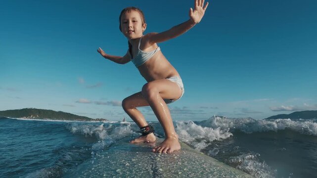 Kid surfs. Little girl learns surfing and tries to keep balance on the surf board