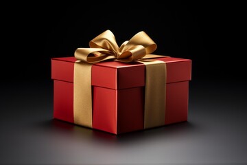 Obraz premium Red gift box wrapped with gold ribbon and bow resting on a dark surface