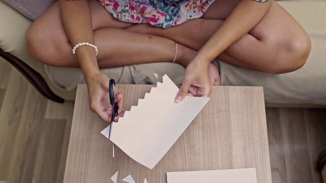 A close-up view of hands carefully using zig-zag scissors to cut white paper, creating a decorative border. Perfect for illustrating DIY projects, hobbies, and artistic endeavors.