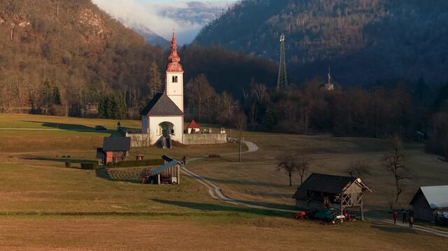 Close aerial flyover traditional kozolec hayracks and red church roof Bitnje village Bohinj valley Slovenia Julian Alps sunset minimalist travel destination dji air 3s 10-bit 4k