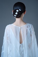 Elegant woman back view wearing white dress with floral hair accessory.