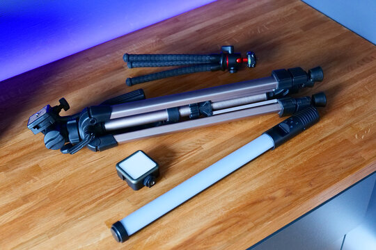 Photography equipment including tripods, LED lights, and light stands arranged on a wooden surface with a modern backdrop featuring purple lighting