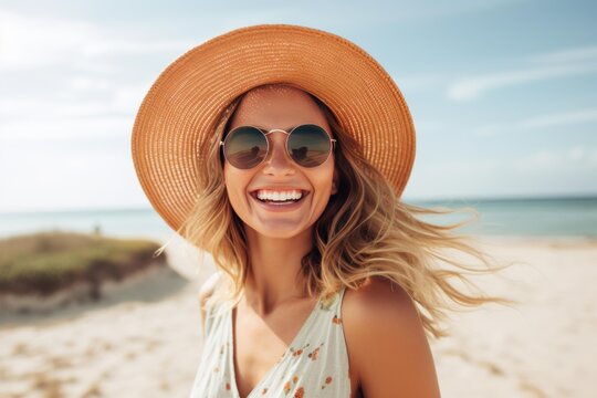 Woman wearing straw hat and sunglasses laughing on a sandy beach