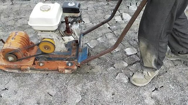 Road worker compacting a cobblestone sidewalk with a gasoline plate compactor machine