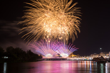 Colorful fireworks lighting up the night sky above the Mae Klong River in Ratchaburi Province, Thailand, creating a festive and celebratory atmosphere, suitable for celebration themes.