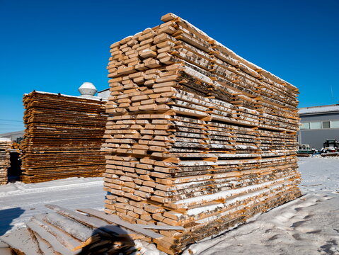 Stacks of lumber in a snowy yard during winter in a timber processing area