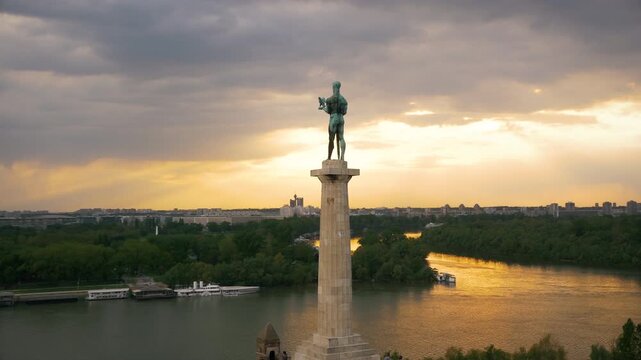 Cinematic wide drone shot of the Victor (Pobednik) monument in Belgrade at sunset. Iconic statue overlooking the Sava and Danube confluence at the Kalemegdan fortress.