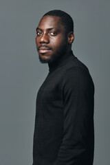 Obraz premium Portrait of African American man with dark skin wearing black turtleneck sweater looking at camera with confident expression in creative visual designer style on gray background.
