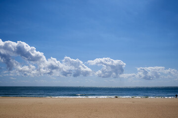 Fototapeta premium Peaceful landscape of the wide sandy Haeundae Beach under a bright blue sky with scattered white clouds in Busan, South Korea, during a calm afternoon.