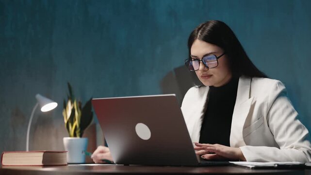 A focused businesswoman works on her laptop in a modern office, concentrating on her tasks, reviewing data, and managing her workload efficiently in a professional environment.
