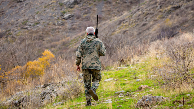 A hunter in camouflage with a rifle stalks game in the mountains. Hunting for game in the mountains. A man with a rifle and dog practices hunting and shooting together in the wild.