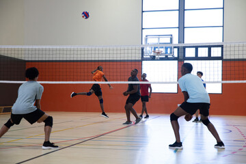 Obraz premium Diverse teenage male players spiking volleyball over net in gymnasium with orange jersey