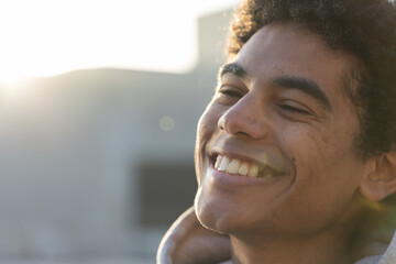 African American man smiling under warm backlight on rooftop, wearing hoodie with lens flare