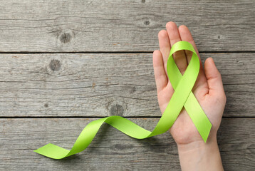 Hand holding vibrant lime green awareness ribbon on rustic wooden background for mental health