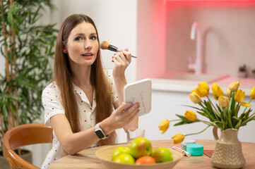 Long-haired beautiful young woman with a face brush sitting at the table