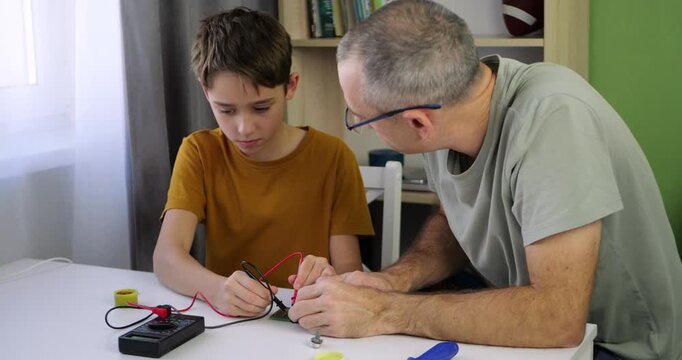 Child explores electronics during home stem class. Father supports testing with multimeter and guides experiment. Family project builds science skills. Stem learning creates creative atmosphere.
