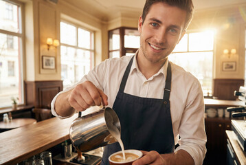 Smiling barista in white shirt adds frothed milk to coffee cup in cozy cafe setting