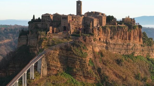 Civita di Bagnoregio Aerial: Cinematic 70mm Drone Flight Towards Ancient Hilltop Village, Misty morning Mountains Backdrop, Historic Footbridge, Lazio Italy, Tuscia viterbese iconic landmark 4K