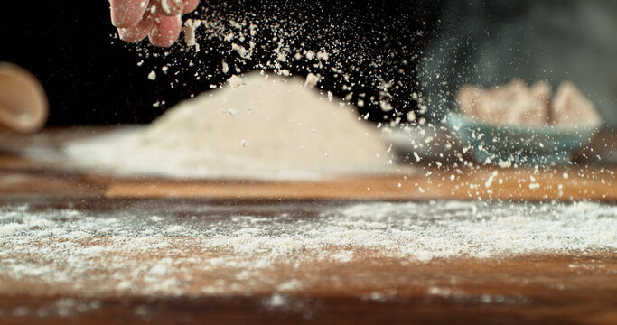 Close up of baker&rsquo;s hand tossing flour over prepared risen dough on wooden table. Cinematic baking concept, artisan bread preparation and texture detail.