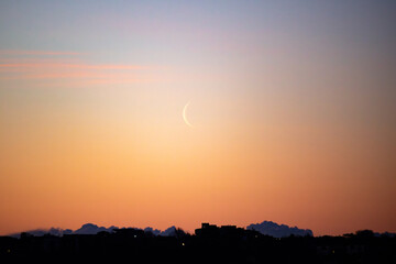 Fototapeta premium Crescent moon rising at dawn over south Dublin against a golden orange sky
