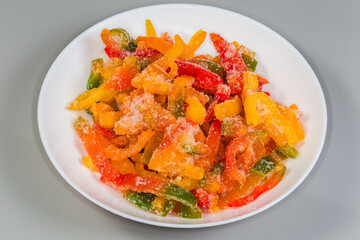 Fototapeta premium Frozen sliced multicolored bell peppers on dish on gray background