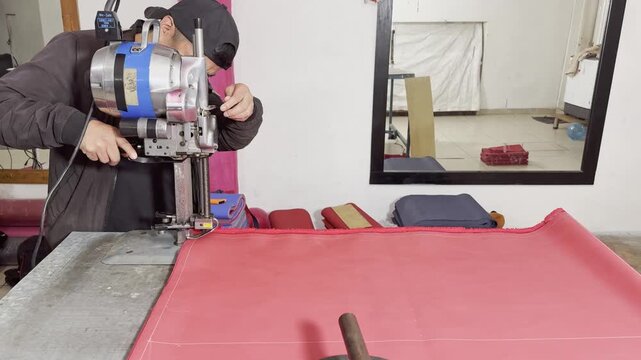 Professional tailor using electric cloth cutting machine on red fabric.