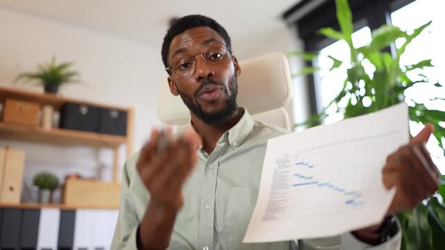 Confident businessman presenting financial report to camera in modern office, explaining charts and data during online meeting. Professional, focused and engaging communication