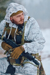 Obraz premium Soldier In Winter Camouflage With Rifle And Tactical Gear Kneeling In Snow During Patrol