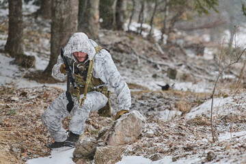 Fototapeta premium Soldier In White Winter Camouflage Patrolling Snowy Forest With Rifle During Cold Weather Operation