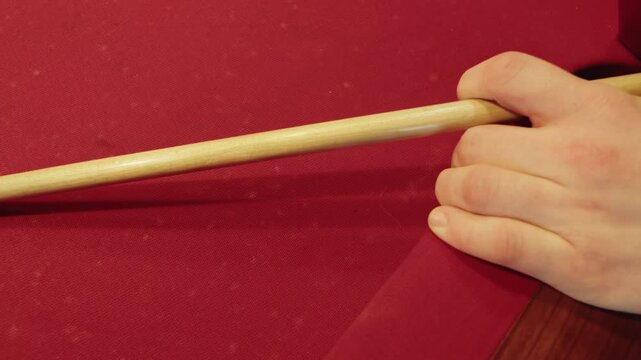 Close up of stance aligning chalked cue tip relatively ball placement during practice. Top view of meticulous male hand positioning ensuring white cue ball contact on a red felt table